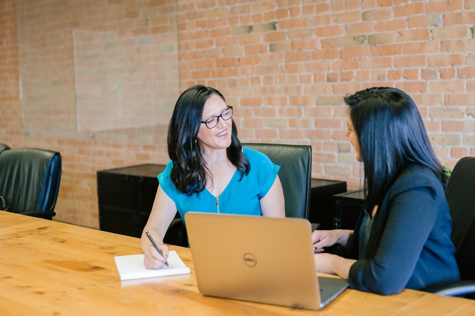 Priya, an underwriter, talks through a file with a colleague at a wooden table