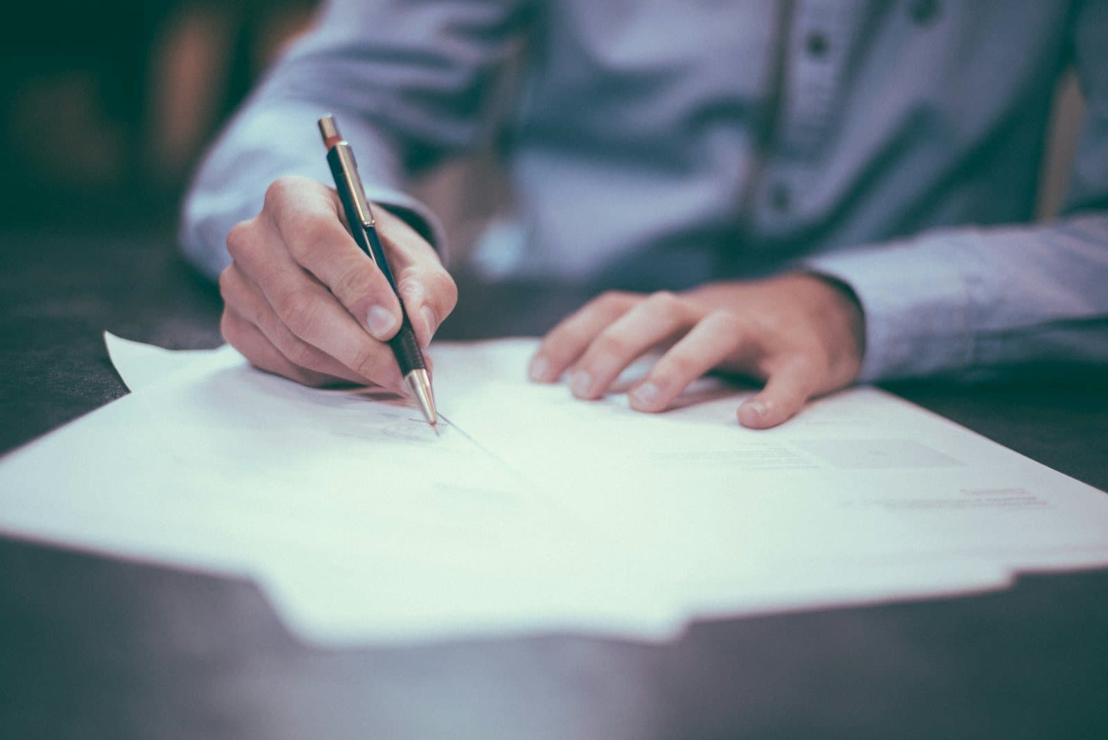 A hand signs a printed document with a fountain pen